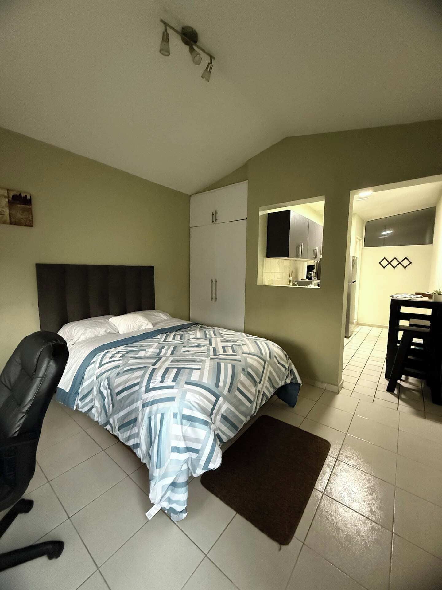 Quarto com cama, escrivaninha, cadeira, guarda-roupa e banheiro pequeno.