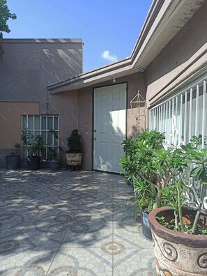 A building with a tiled patio, a white door, and potted plants.