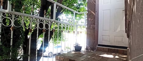 A staircase leading to a door with a white door, surrounded by greenery and a metal railing.