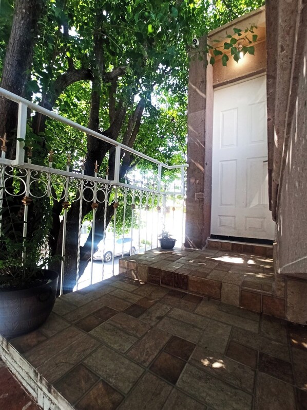 A staircase leading to a door with a white door, surrounded by greenery and a metal railing.