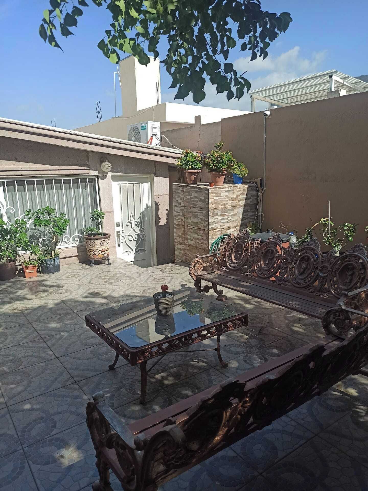 An outdoor patio with a glass table, potted plants, and a decorative metal fence.
