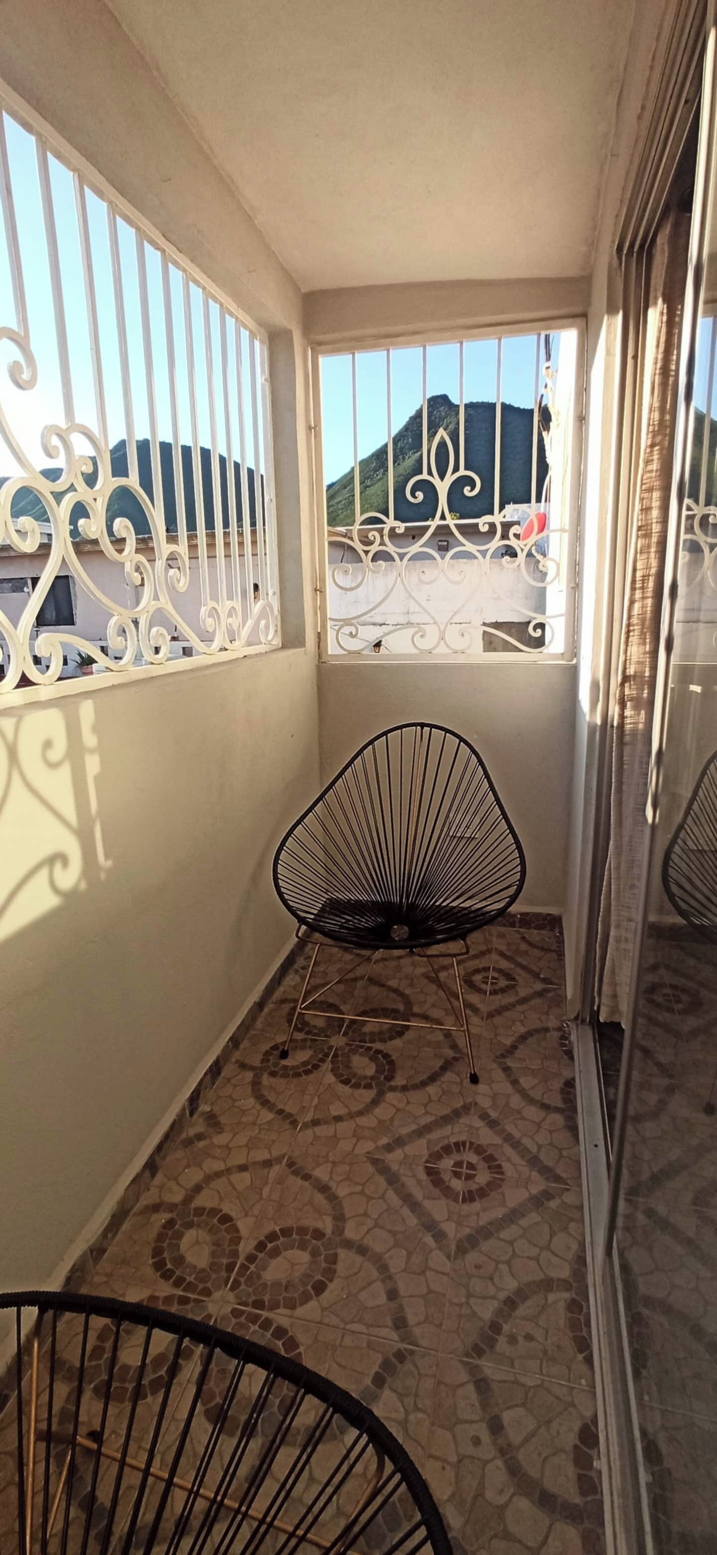 A balcony with patterned floor tiles, a black chair, and a window with decorative metal bars.