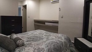 Een slaapkamer met een bed, dressoir, spiegel en een ingebouwde airconditioning.
