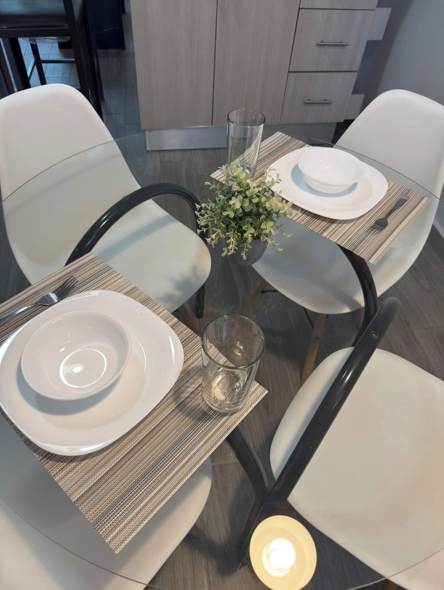 A dining table set with plates, cutlery, and a glass, surrounded by chairs with a woven placemat.