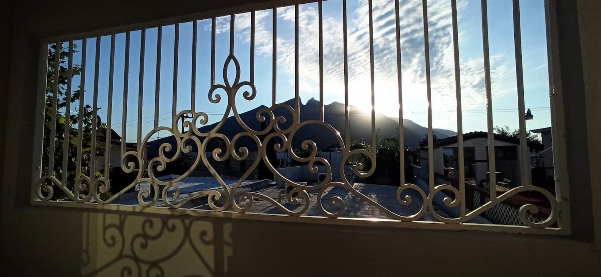 Une fenêtre ornée de barreaux en métal ouvragé, donnant sur une chaîne de montagnes.