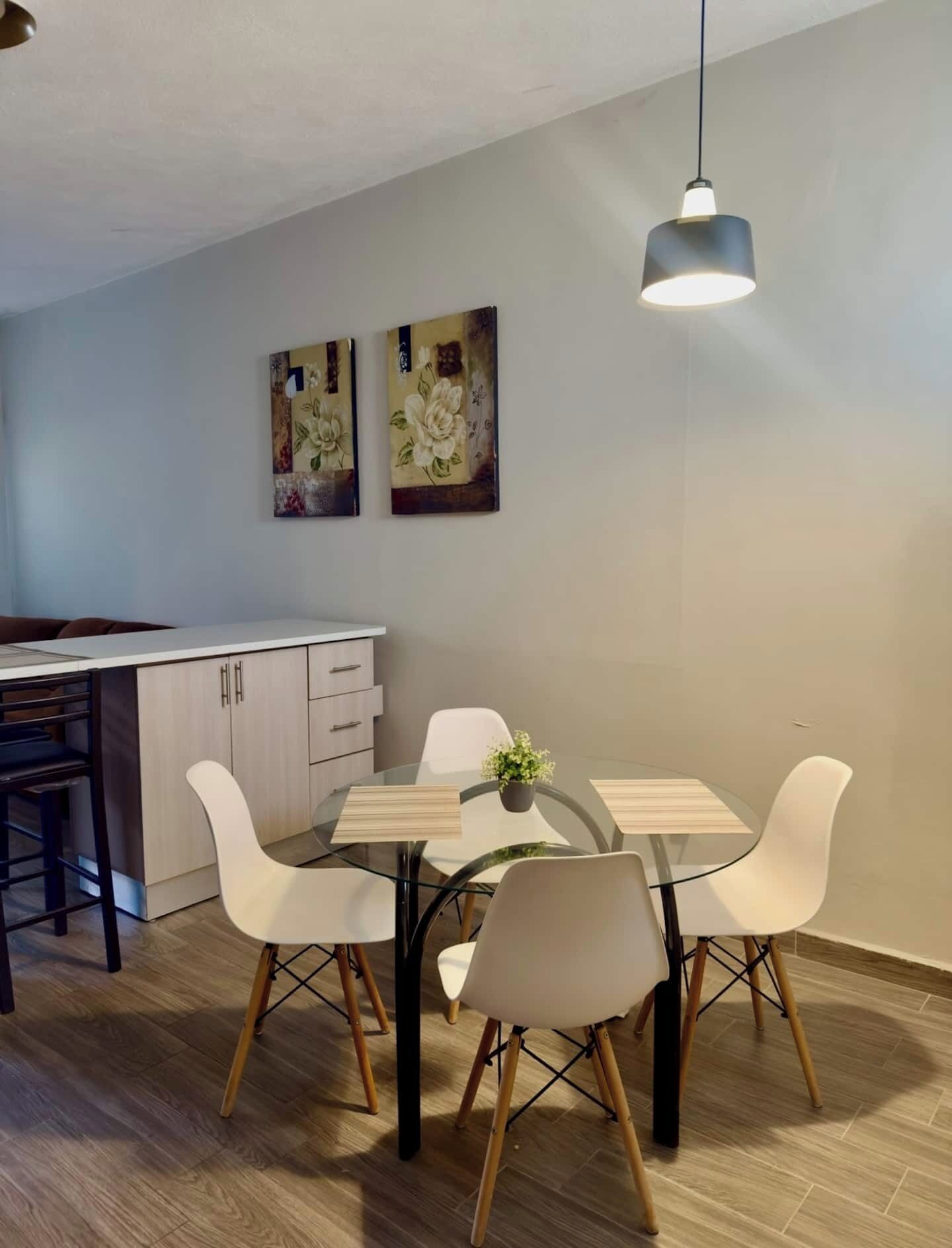 Een moderne keuken met een eethoek, voorzien van een tafel met stoelen, een hanglamp en twee aan de muur bevestigde schilderijen.