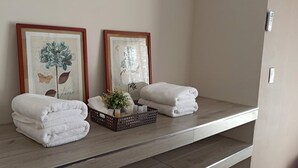 Een badkamer met twee ingelijste plantendrukken, een stapel witte handdoeken en een kleine plant op een plank.