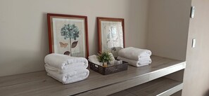 A bathroom with two framed botanical prints, a stack of white towels, and a small plant on a shelf.