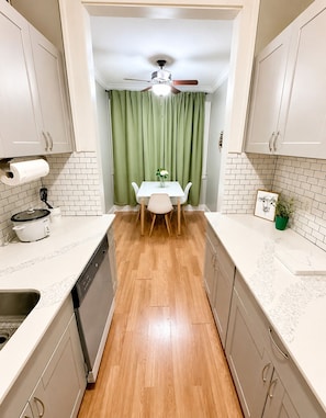 A compact kitchen with white cabinets, a dining table with chairs, a ceiling fan, and a green curtain. - Charming Downtown Studio - Walk to Toyota Center (Houston)