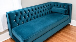 A teal velvet sofa with tufted backrest and armrests, positioned against a white wall and wooden floor. - Charming Downtown Studio - Walk to Toyota Center (Houston)