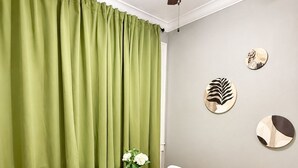 A dining area with a white table, two chairs, a vase with flowers, green curtains, a ceiling fan, and wall art. - Charming Downtown Studio - Walk to Toyota Center (Houston)