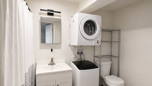 Et lille badeværelse med en hvid vask, toilet, vaskemaskine og spejl.