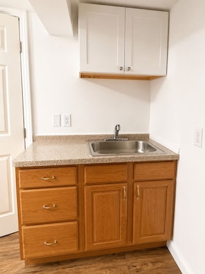 A kitchen with a granite countertop, wooden cabinets, a stainless steel sink, and a white ceiling. - Spacious Studio Near Boston--Parking--Washer/Dryer (Everett)
