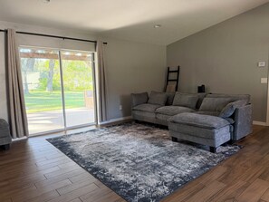 A living room with a grey sectional sofa, a patterned rug, and a sliding glass door leading to a yard. - 3-bedroom house near Brownwood • Pet Friendly (Wildwood)