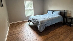 Una camera da letto con un letto, una finestra con persiane, una lampada a soffitto e pavimento in legno.
