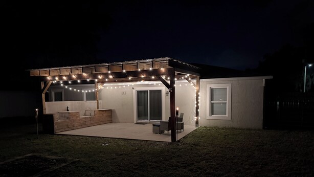 Un'area patio esterna coperta con luci a tendina, una panca di legno e una porta scorrevole in vetro che dà su un portico coperto.