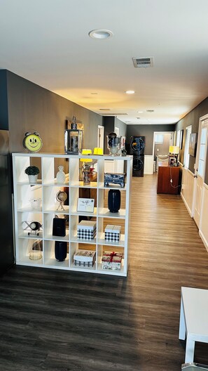 A hotel lobby with a central white shelving unit displaying various items, a wooden floor, and a reception desk in the background. - Fantastic 2-bedroom house with AC in sunny Los Angeles (Los Angeles)