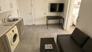 Un ambiente compatto con angolo cottura, lavatrice, TV a schermo piatto, divano e tavolino.