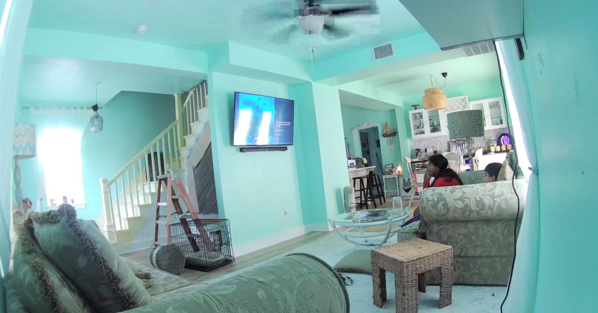 A living room with a sofa, a glass coffee table, a wicker stool, a TV mounted on the wall, and a staircase leading to another level.