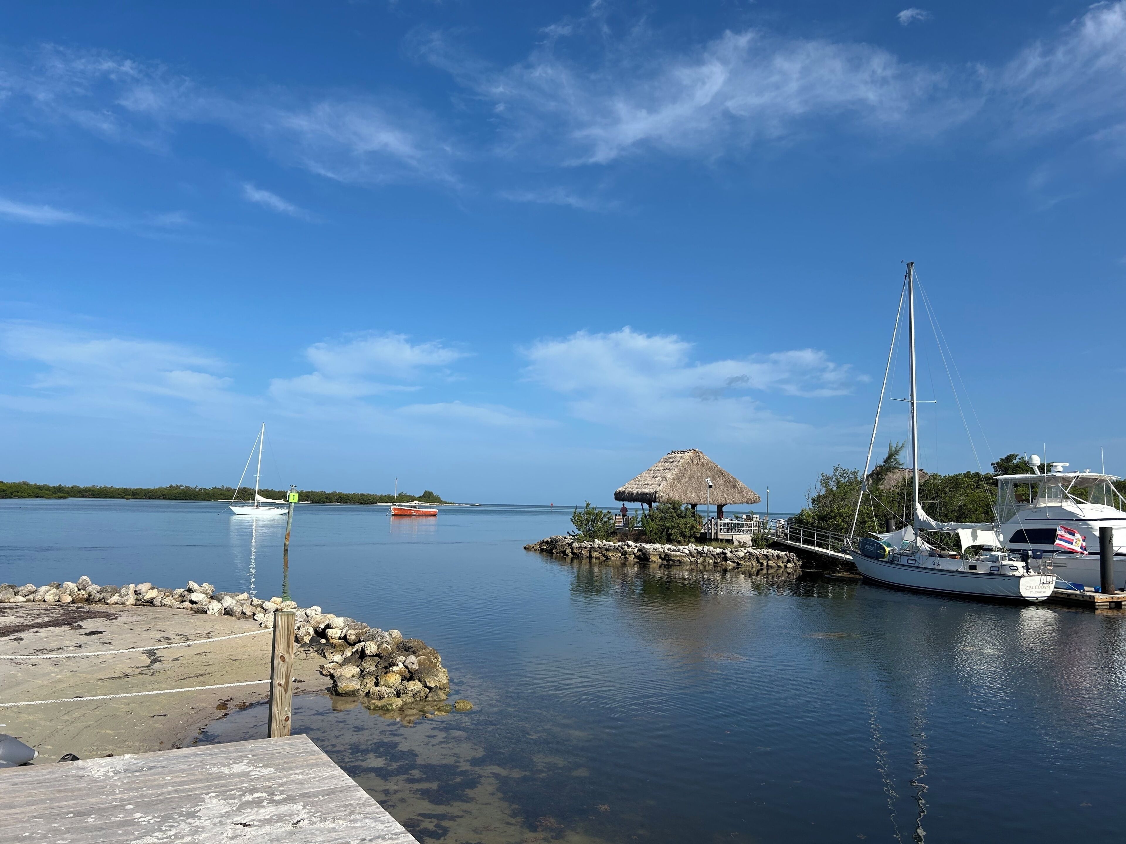 A marina with boats, a thatched-roof structure, and a rocky shoreline.