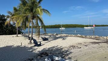 Una playa con palmeras, sillas de descanso, un bote y un canal con barcos.