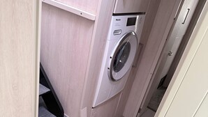 Un área de lavandería compacta con lavadora, un escalón pequeño con un tapete estampado y una puerta que da a otra habitación.