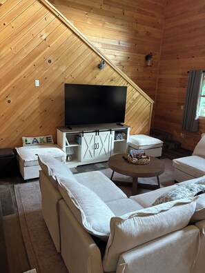 Interior acollidor d'una cabana amb una televisió sobre un moble de fusta, un sofà i una taula rodona petita.
