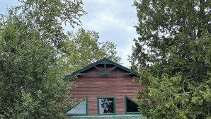 A two-story building with a green roof, a yellow door, and a porch with benches. - Peaceful Schroon Lake getaway with cozy comforts and year-round adventures. (Adirondack)