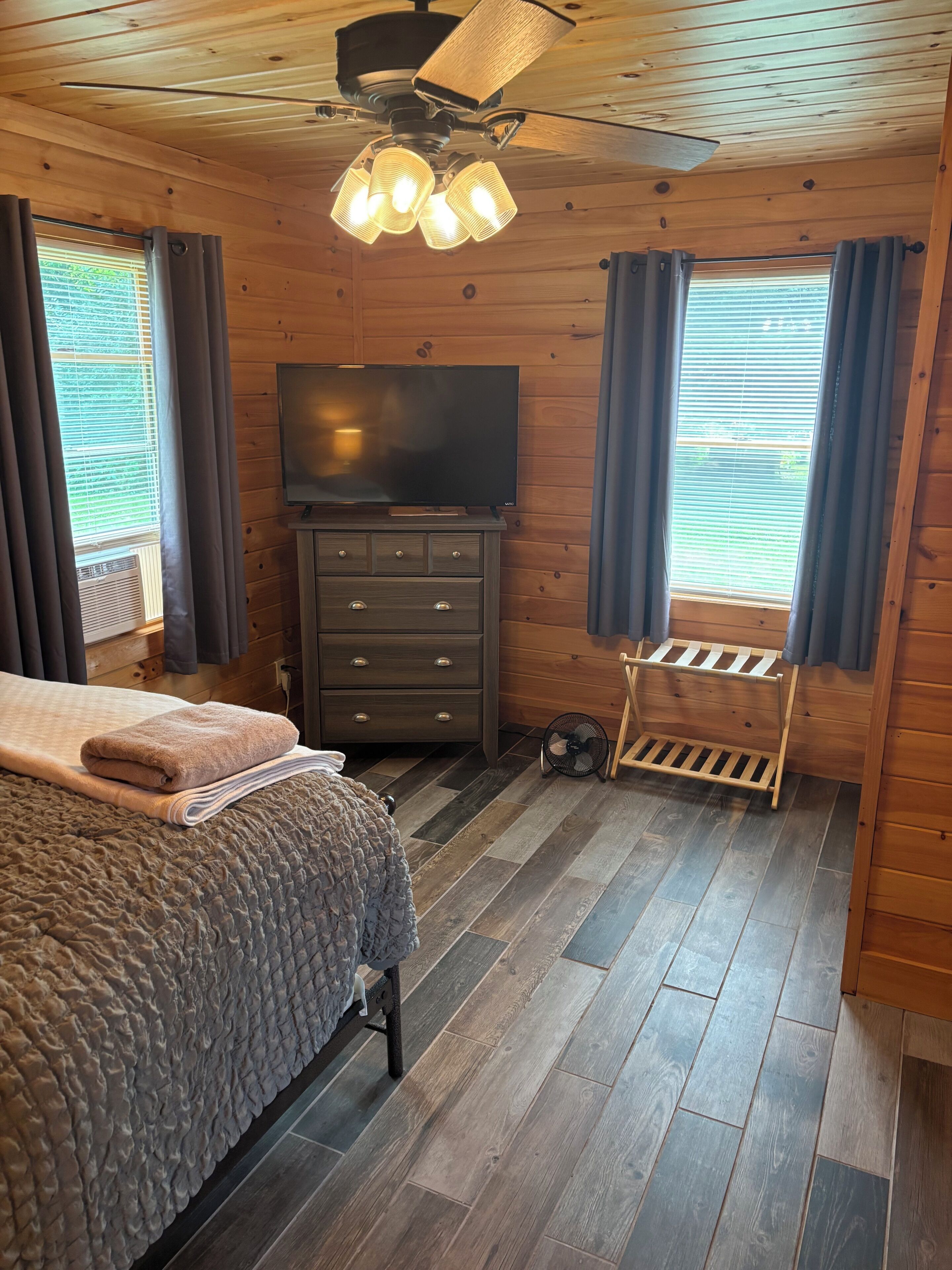 A bedroom with a bed, a TV, a dresser, and a ceiling fan.