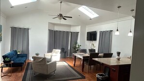 Un'ampia zona living con ventilatore a soffitto, un tavolo da pranzo con sedie, un divano e una TV fissata al muro.