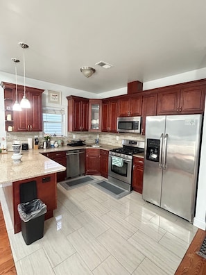 A modern kitchen with wooden cabinets, stainless steel appliances, and a granite countertop. - Bright 3BR &2 Bath! Easy Trip to NYC l Parking (Jersey City)