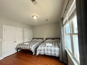 Ein Zimmer mit zwei Betten, einem Vorhangfenster und einer Tür.