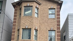 Una casa a due piani in mattoni con un garage, un portone d'ingresso con un pannello di vetro decorativo e un SUV nero parcheggiato nel vialetto.