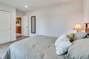 A bedroom with a bed, pillows, a lamp, a mirror, and a door leading to a kitchen. - Grants Pass Retreat Across from Riverside Park! (Grants Pass)