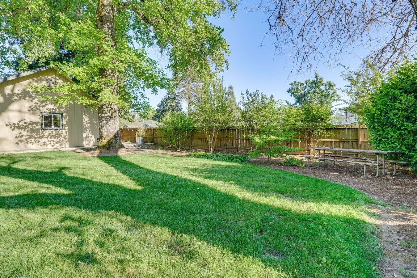 Ein Garten mit Holzzaun, Picknicktisch und einem Haus mit Fenster.