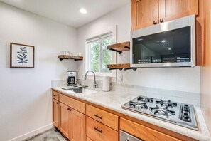 A kitchen with wooden cabinets, a stainless steel stove, a coffee maker, and a window. - Grants Pass Retreat Across from Riverside Park! (Grants Pass)