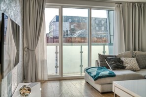 Ein modernes Wohnzimmer mit einer Couch, einem Fernseher und einem Balkon mit Blick auf Gebäude.