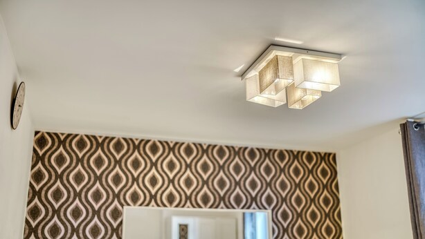 Una habitació amb paper pintat, un mirall rectangular i una làmpada al sostre.