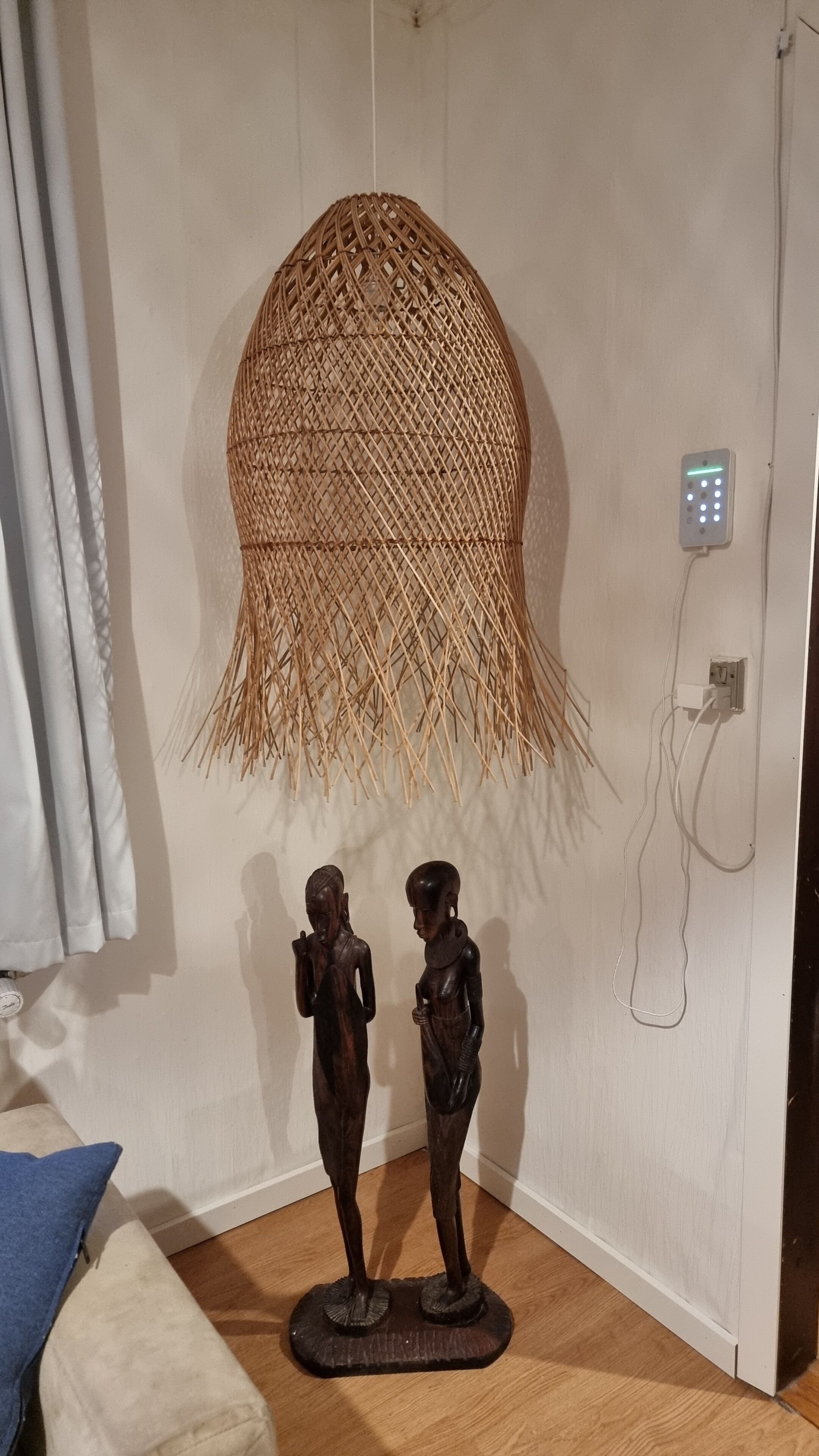 Une pièce dans laquelle on peut voir un panier tressé accroché au mur, une prise de courant et deux sculptures en bois posées sur le sol.