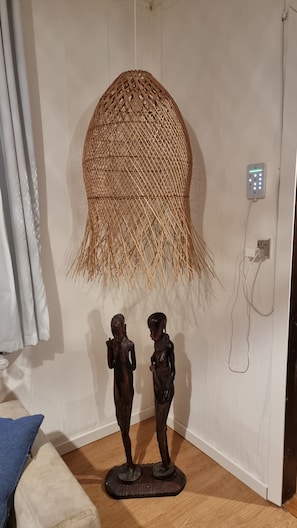 A room with a woven basket hanging on the wall, a power outlet, and two wooden sculptures on the floor.