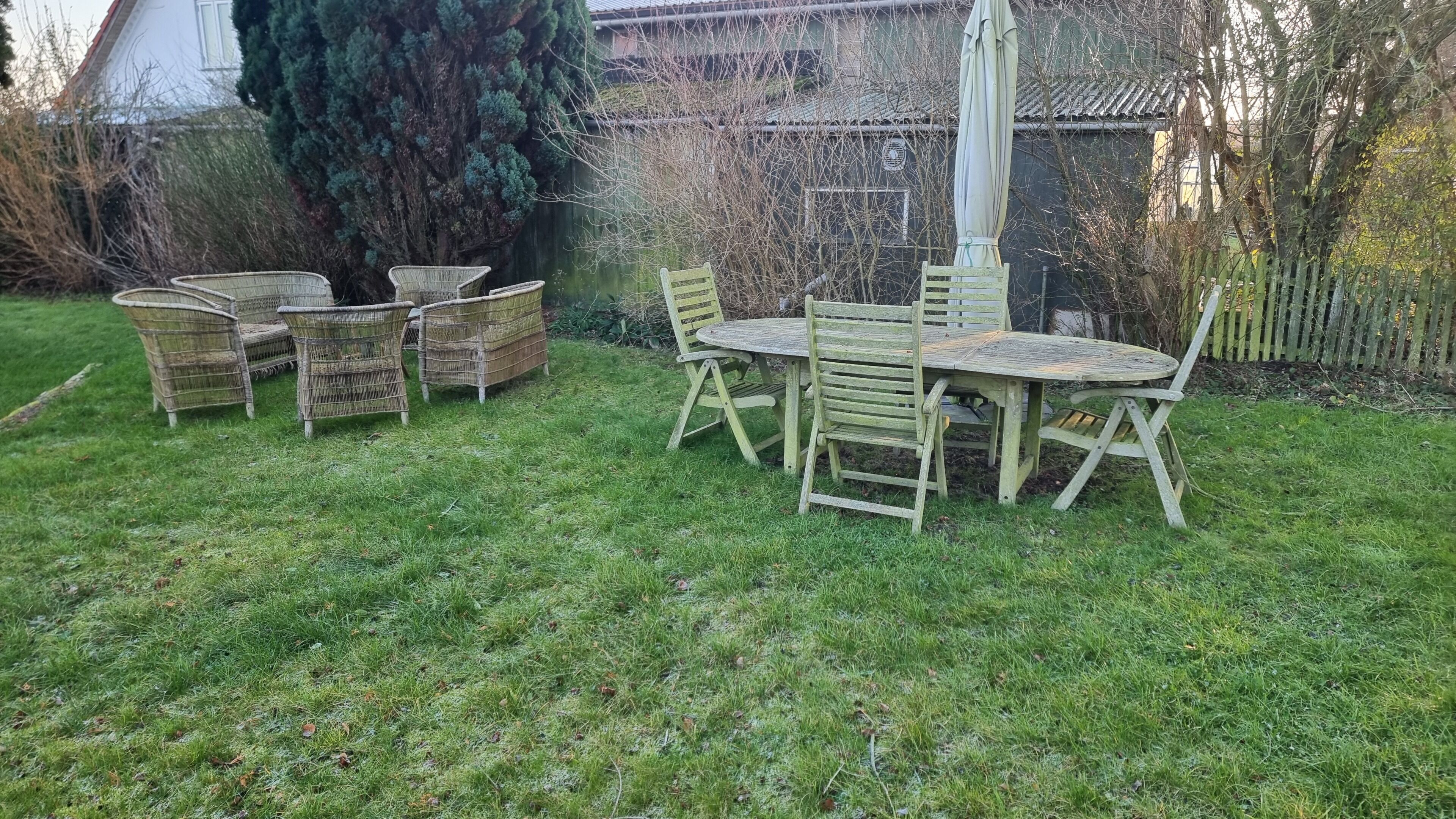 Un jardín con mesa y sillas de madera, rodeado de césped y árboles.