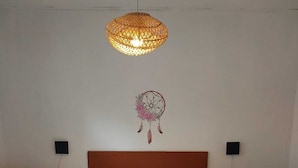 Un dormitorio con una cama de madera, dos mesitas de noche, un atrapasueños colgado en la pared y una lámpara colgante.