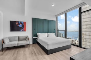 A modern bedroom with a bed, a sofa, a large window, and a city view. - Skyline Miami & Resort Amenities (Miami)