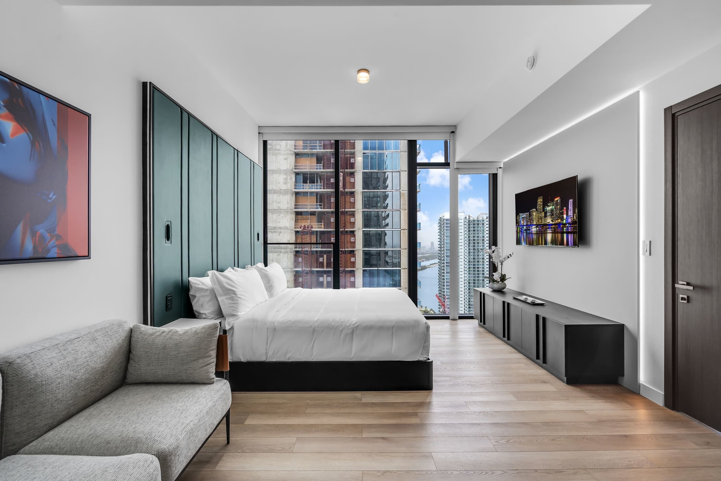 Een moderne slaapkamer met een groot bed, een bank, een televisie en uitzicht over de stad.