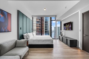 A modern bedroom with a large bed, a sofa, a TV, and a city view. - Skyline Miami & Resort Amenities (Miami)