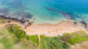 Vista aérea de una playa con agua cristalina, arena dorada y abundante vegetación verde.