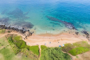Eine Luftaufnahme eines Strandes mit klarem Wasser, sandigem Ufer und grüner Vegetation.