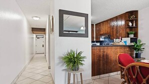 Un pasillo que da a una cocina con armarios de madera, un comedor con una silla roja y una planta en maceta.