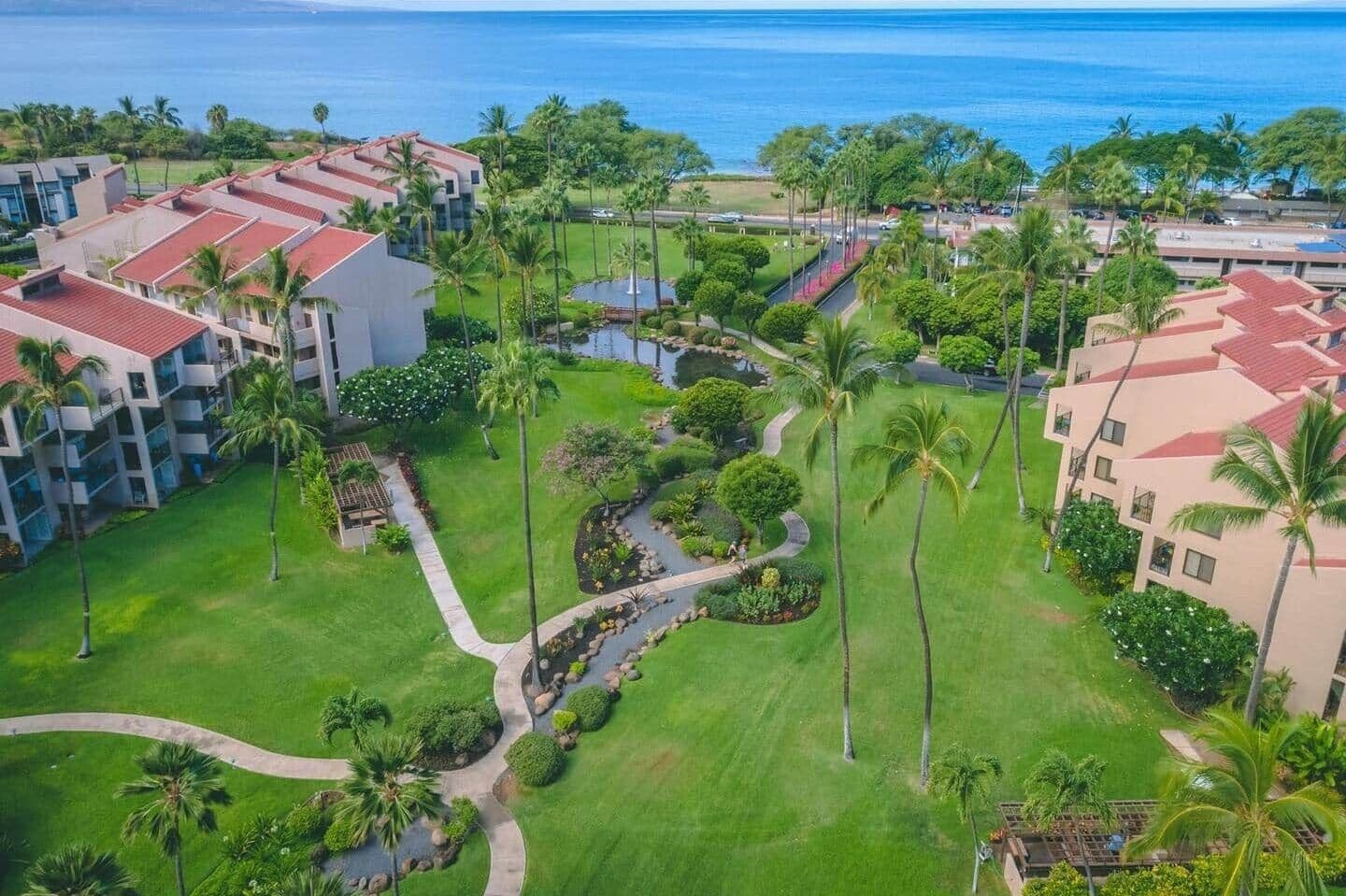Un resort con varias edificaciones, palmeras y un sendero que lleva a una fuente de agua.