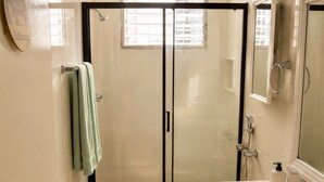 A bathroom with a glass shower enclosure, a toilet, a sink, and a mirror.